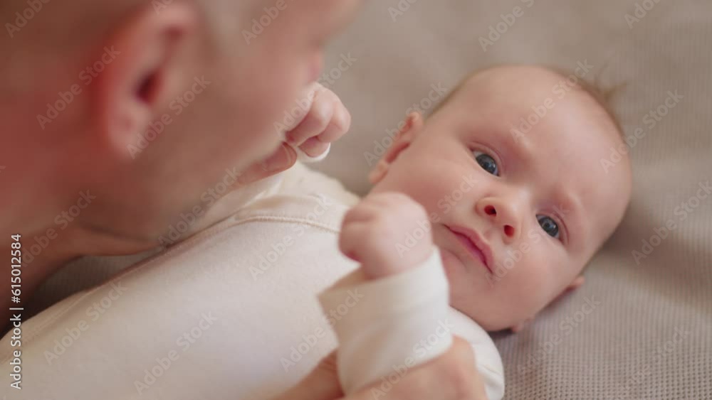 Dad playing and kissing with a newborn baby. Cute baby is trying to pronounce sounds while looking at his dad. Face of an active Caucasian baby looking at a parent. Father is kissing his baby. Dad playing and kissing with a newborn baby. Cute baby is trying to pronounce sounds while looking at his dad. Face of an active Caucasian baby looking at a parent. Father is kissing his baby.