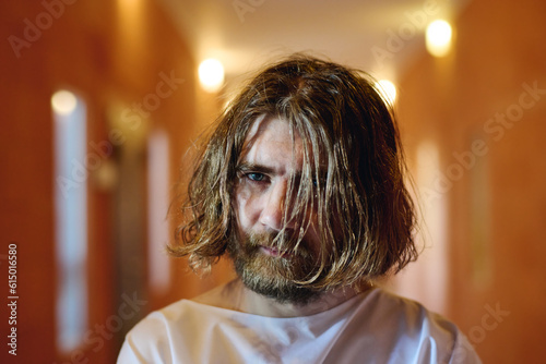 Schilderij op canvas Young bearded male patient of mental hospital with long blond shaggy hair standi