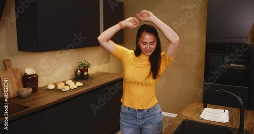 Smiling young woman working online on a laptop and dancing in her kitchen at home