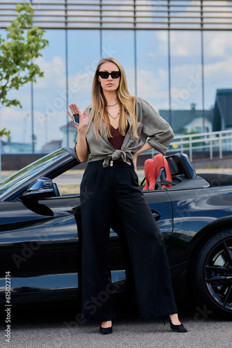 As the epitome of accomplishment, a woman stands beside her shiny new convertible, the embodiment of her relentless pursuit of success and luxury © makedonski2015