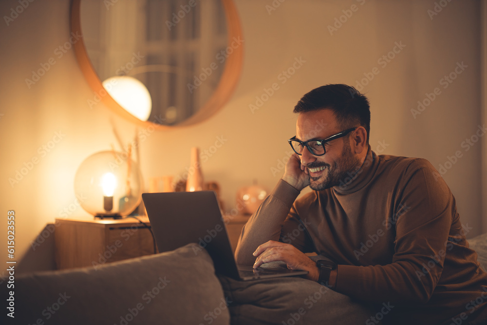 Positive man spending night at home, enjoying the evening, using a laptop.