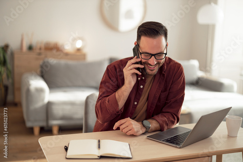 Positive man talking to one of his friends, wearing glasses, sitting at his home office.