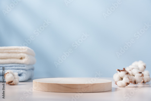 Wooden round podium pedestal. Product presentation  on blue background with cotton towels and branch of cotton