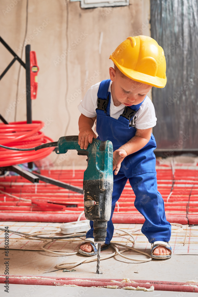 Child in safety helmet drilling floor with electric hammer drill at