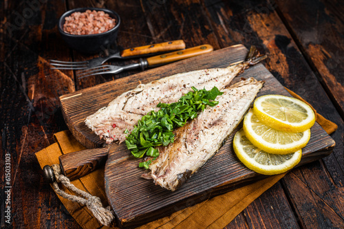 Delicious baked mackerel fillets with greens, garlic and lemon on wooden board. Wooden background. Top view