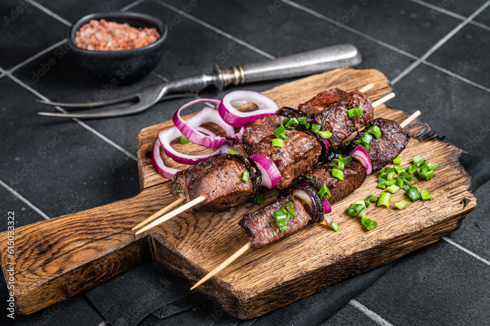Shashlik grilled meat skewers, shish kebab with beef and lamb meat, onion and herbs. Black background. Top view