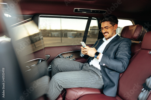 Young elegant businessman sitting on the back seat of a luxury car and using smartphone © fotofabrika