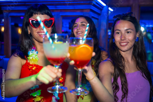 Female friends in a nightclub toasting with glasses of alcohol smiling at a night party