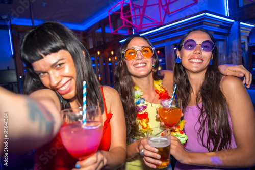 Fun of friends smiling with glasses of alcohol in a nightclub taking a selfie at a night party photo