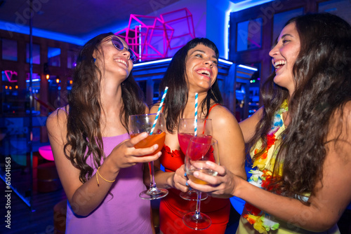 Portrait attractive women toasting and having fun with drinks in disco club at summer night party in pub