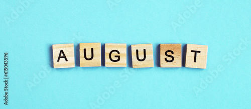 August word made by wooden cubes on a blue turquoise background.