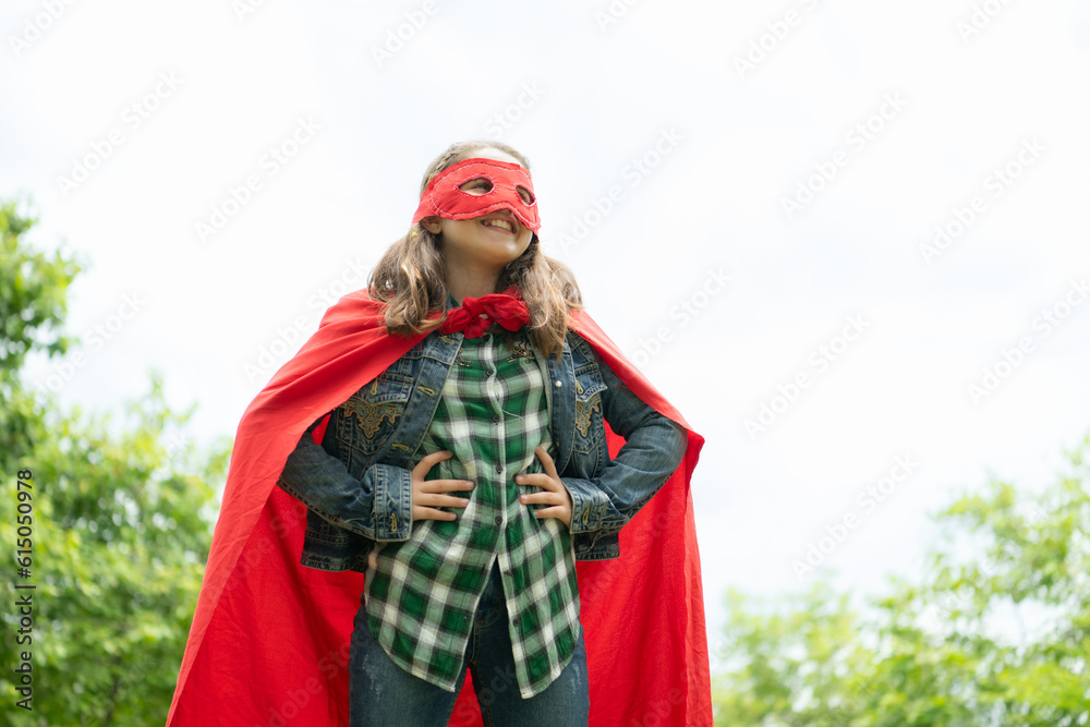 On a beautiful day in the park, a young girl enjoys her vacation. Playful with a red superhero costume and mask.