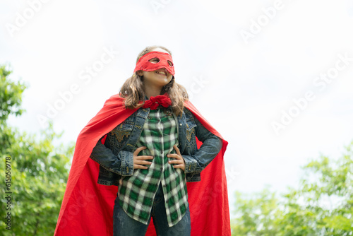 On a beautiful day in the park, a young girl enjoys her vacation. Playful with a red superhero costume and mask.