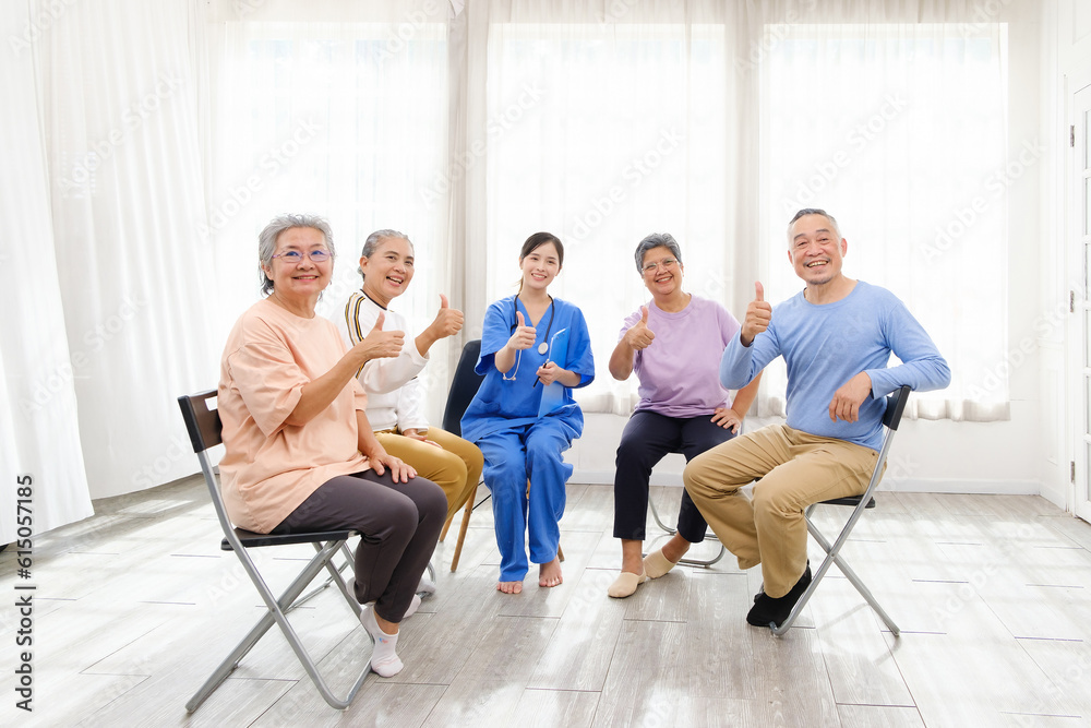 Fototapeta premium The caregiver therapist sits with a group of Asian senior people with thumbs up in a circle for checking physical and mental health in a group elderly therapy session. The nursing home facilitates