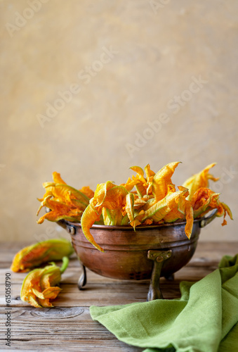 Zucchini flowers in a brass colander with green napkin. Vertical shot, wooden table, copy space for text