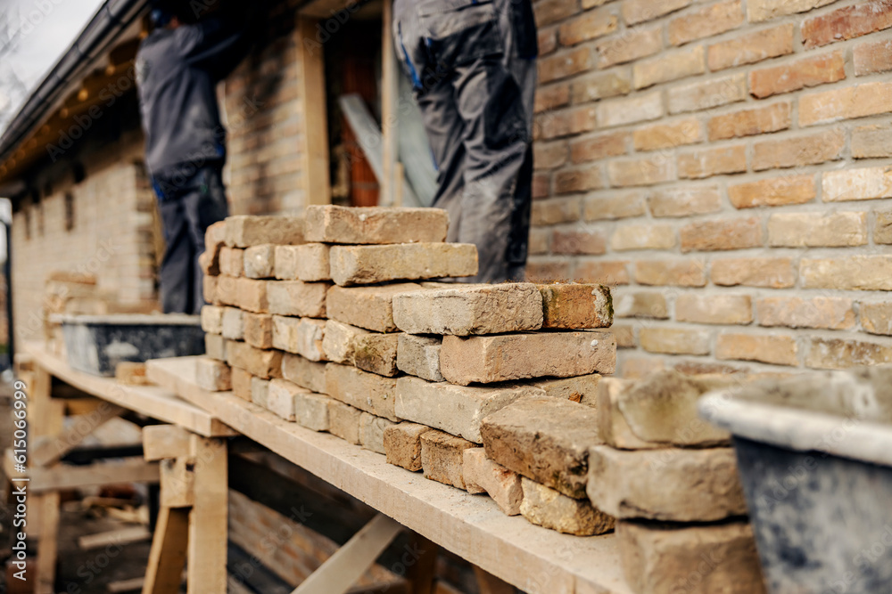 Selective focus on pile of bricks on a scaffolding with builders making a house. Selective focus on pile of bricks on a scaffolding with builders making a house.