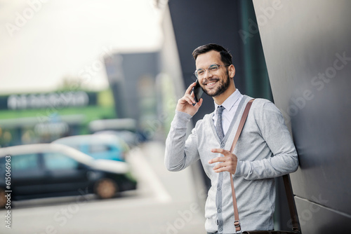 A young happy manager is standing at financial district downtown and talking on the phone.