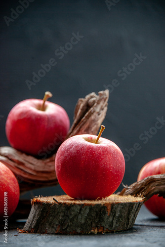 Side view of fresh apples on wooden cutting board and tree branch on dark wave background