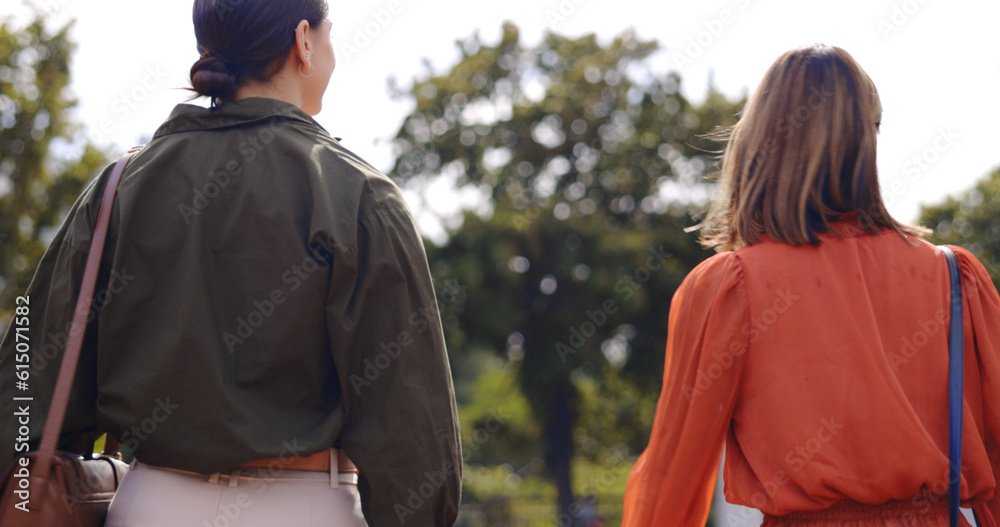 Nature, walking and women friends in conversation while bonding and spending quality time together. Talking, outdoor and back of females speaking while on a walk in a outside green garden or park.