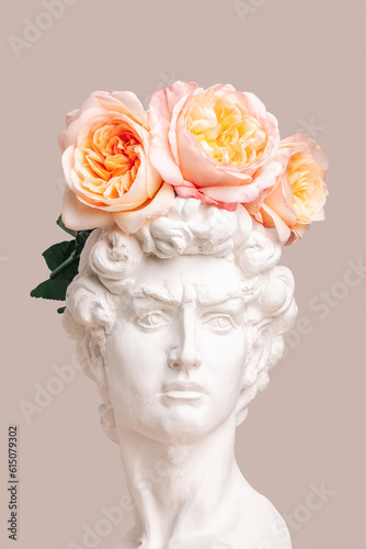 Gypsum copy of the sculpture David Michelangelo with pink peony roses on his head on a beige background