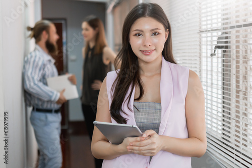 portrait asian confident businesswoman standing in modern office holding digital tablet with businesspeople background. Female smiling manager looking at camera smart lady attractive in company. © eakgrungenerd