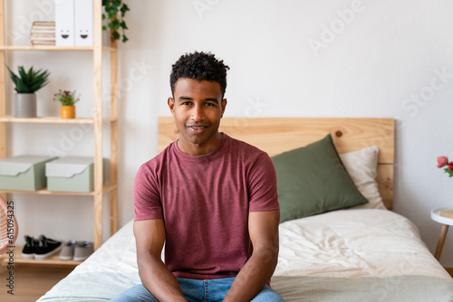 Young man sitting on bed in house with minimalist decor.