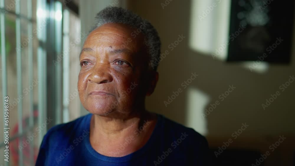 One contemplative black Brazilian senior woman standing by window looking out. A pensive African American elderly person in contemplation, close-up face
