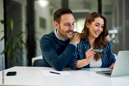 A man hugging his female colleague while she doing online shopping on a laptop.