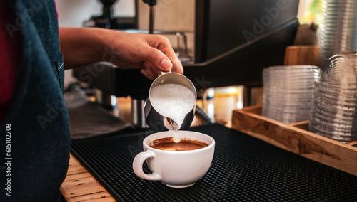 Hand of a barista pouring milk into coffee making cappuccino. Professional barista preparing coffee on the counter.