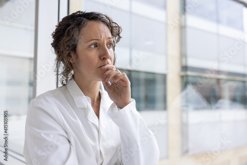 Worried and stressed female doctor looking out of the window in a hospital photo