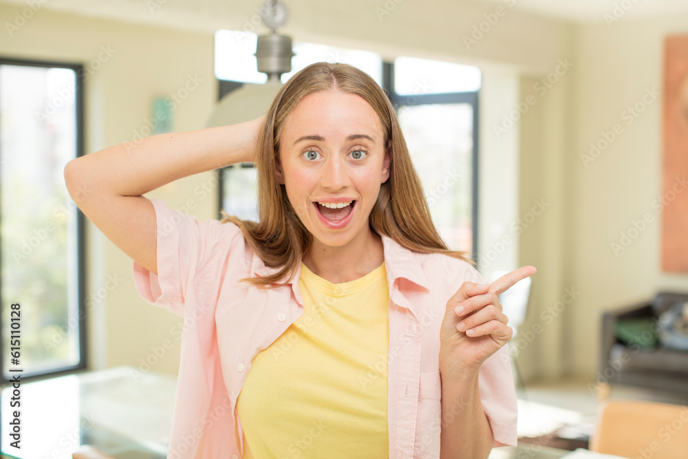 pretty blond woman laughing, looking happy, positive and surprised, realizing a great idea pointing to lateral copy space