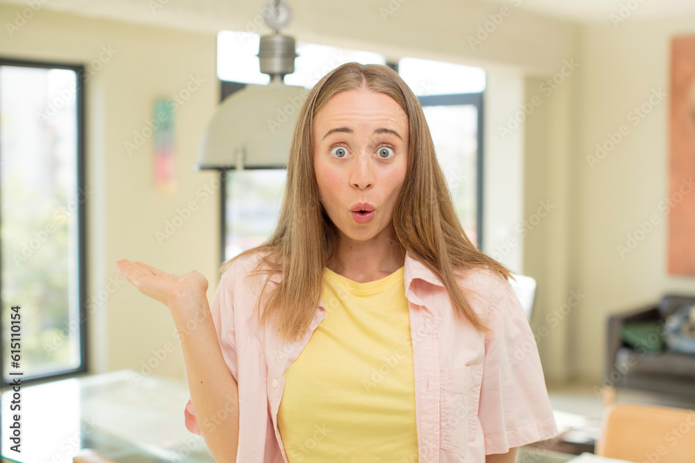 pretty blond woman looking surprised and shocked, with jaw dropped holding an object with an open hand on the side