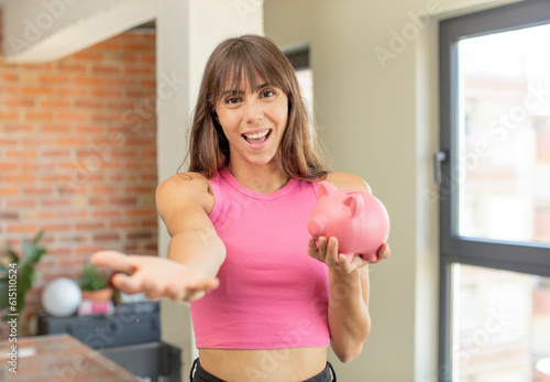 young pretty woman smiling happily and offering or showing a concept piggy bank concept
