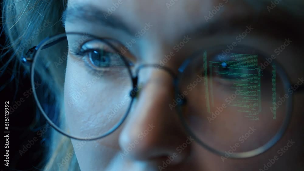 Extreme close up of woman sitting at desk coding in computer program wearing glasses with reflection of screen Extreme close up of woman sitting at desk coding in computer program wearing glasses with reflection of screen