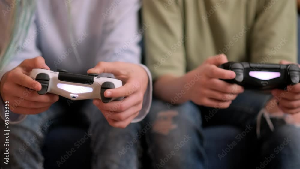 kids hands with joysticks, two children siblings playing video game console while sitting at home, real people, leisure concept.