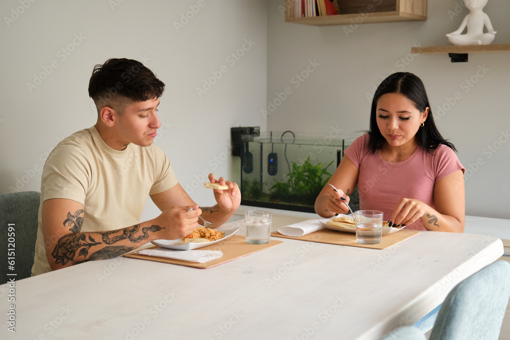 Two young hispanic people eating traditional arepas in the living room.