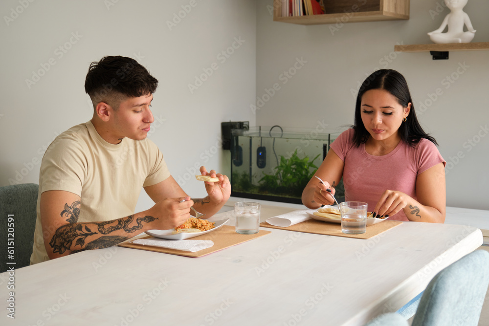 Two young hispanic people eating traditional arepas in the living room. Two young hispanic people eating traditional arepas in the living room.