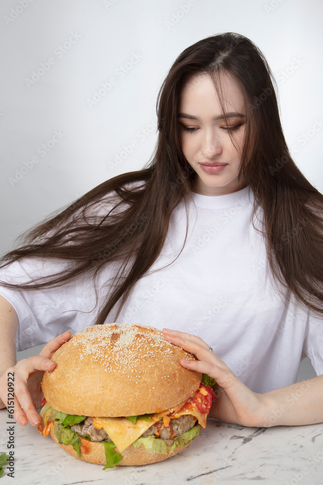 A woman is holding a big barbecue hamburger sandwich on the background. Fast food concept. The girl has a huge hamburger. A woman is holding a big barbecue hamburger sandwich on the background. Fast food concept. The girl has a huge hamburger.