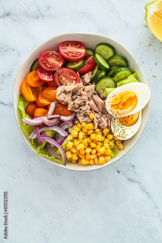 Tuna salad with egg, tomato, cucumber, onion and corn in white bowl, white background.