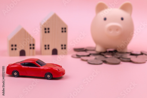 A red car in front of a pink piggy bank on a pile of coin beside the wooden house on pink background. financial for saving and loan, saving money, investment, insurance and leasing concept.