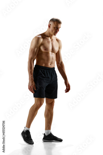 Full-length portrait of handsome young man with relief, fit, strong, ,muscular body standing shirtless against white studio background