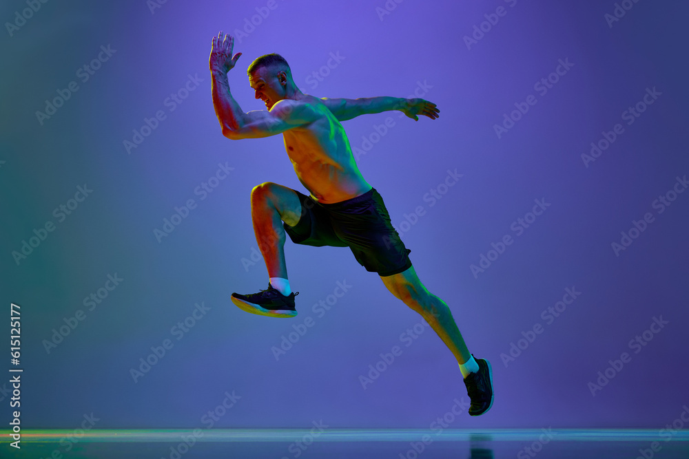 Competitive, motivated man, professional runner, sportsman in motion, training shirtless against blue studio background in neon light