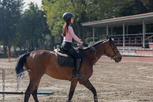 Side shot of a young woman riding a horse in an equestrian center