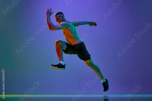 Competitive, motivated man, professional runner, sportsman in motion, training shirtless against blue studio background in neon light
