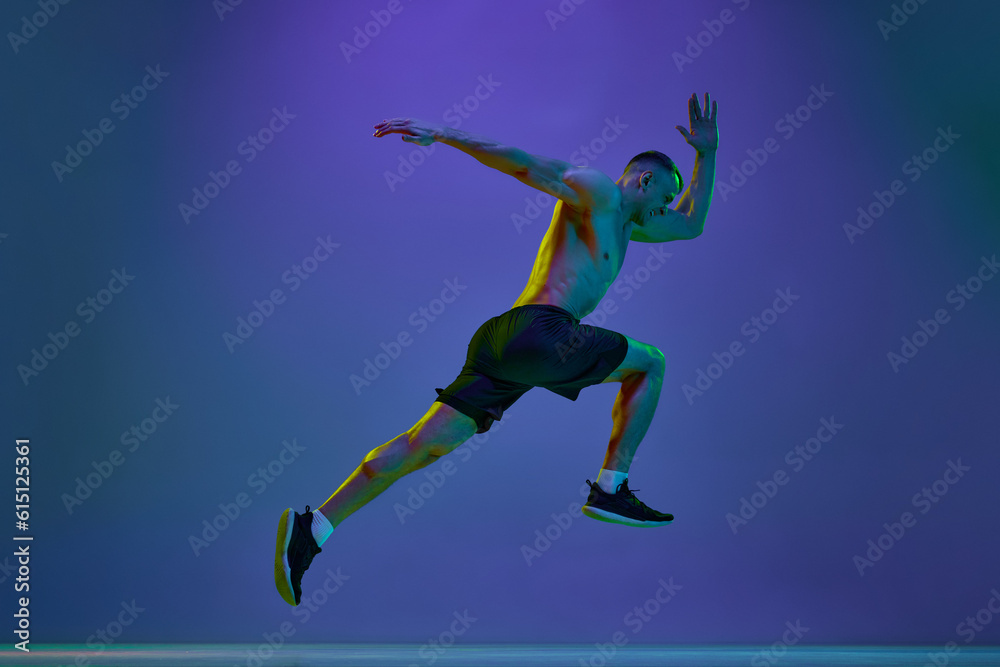 Shirtless man, with fit, relief, muscular body, professional athlete in motion, running against blue studio background in neon light