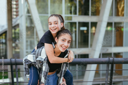 two teenage sisters in the city, one perched on the back of the other