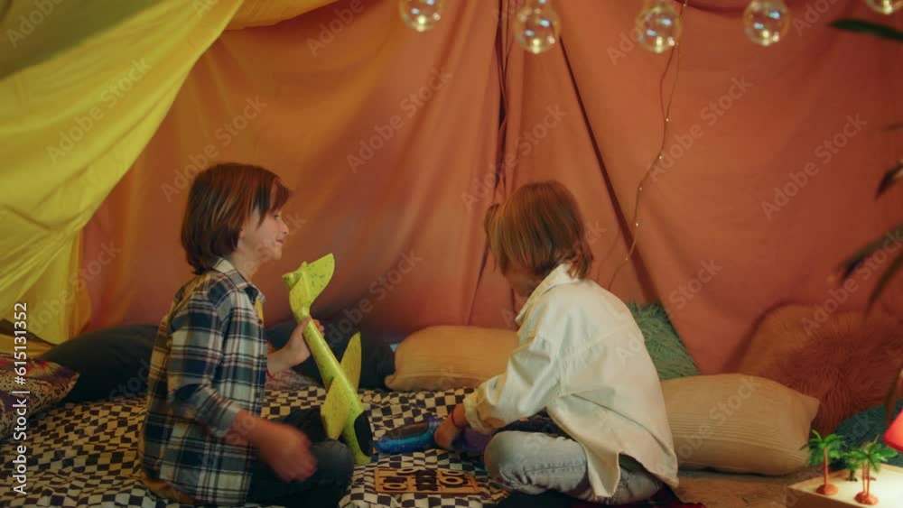 A close up shot of two youthfull buddies playing with airplanes and one of them drops it on the duvet all while being in a massive indoor blanket tent A close up shot of two youthfull buddies playing with airplanes and one of them drops it on the duvet all while being in a massive indoor blanket tent