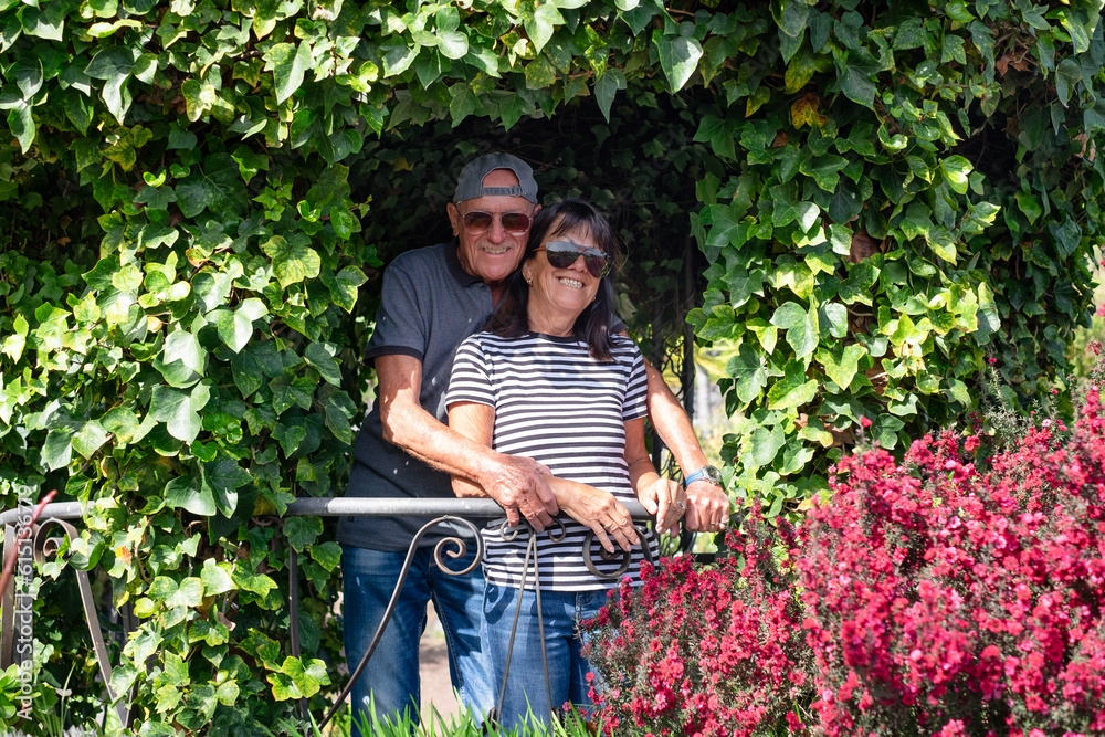 Happy senior family couple in denim and sunglasses hugging in travel vacation relaxing in the garden enjoying beauty in nature Happy senior family couple in denim and sunglasses hugging in travel vacation relaxing in the garden enjoying beauty in nature