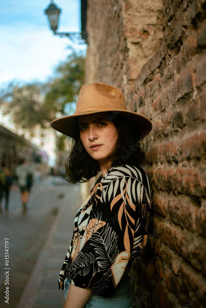 portrait of latin woman leaning on wall of old building looking at camera with a hat on