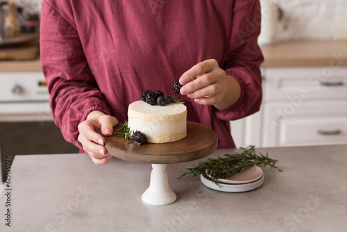 A woman decorates a mini bento cake with blackberries. Beautiful minimalist cake on a wooden stand photo